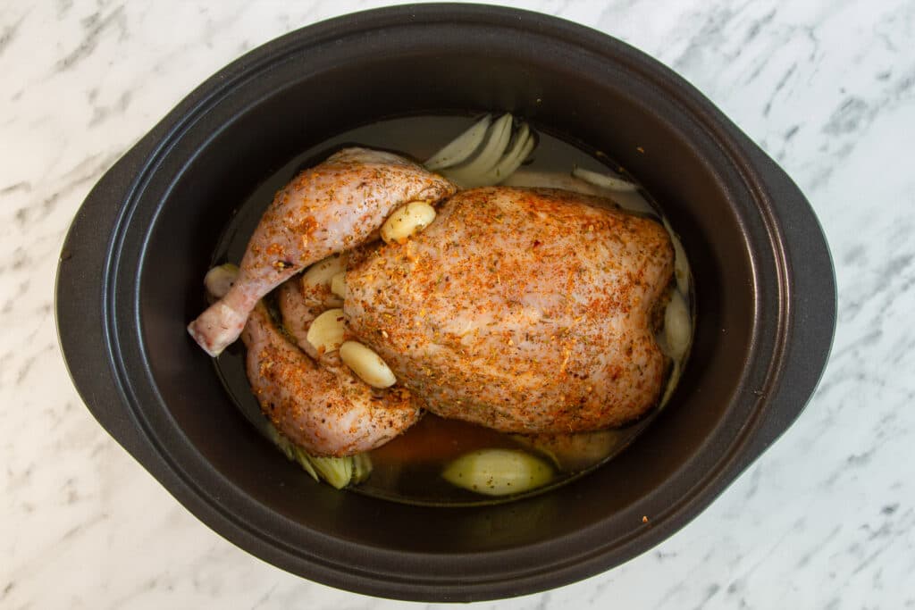 Whole chicken smothered in a rub in a slow cooker.