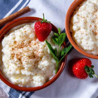 Two bowls of slow cooker rice pudding with mint garnish and strawberries