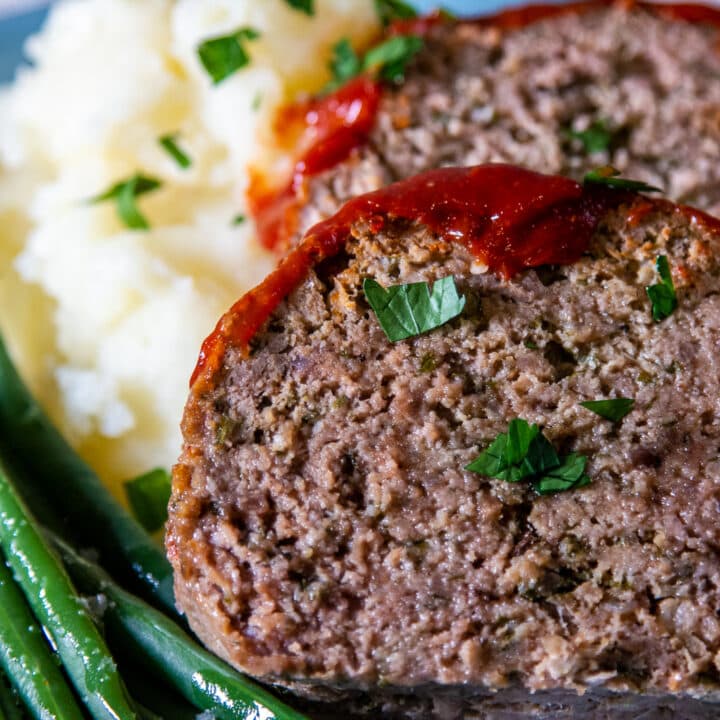 Slices of slow cooker meatloaf on a bed of mash and green beans