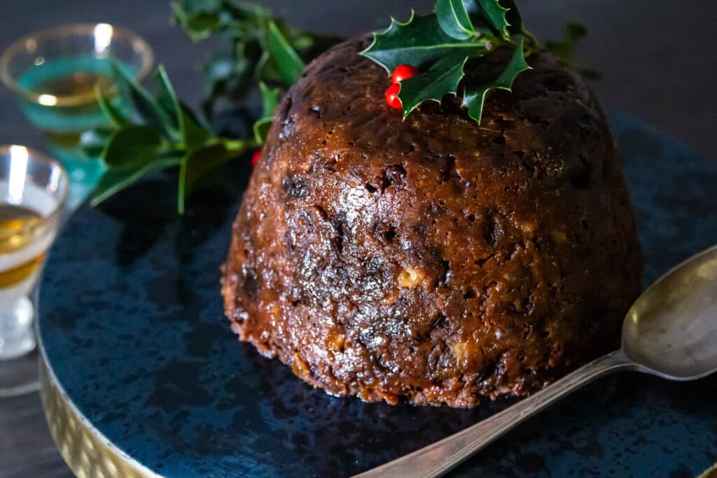 Slow Cooker Christmas Pudding with a tarnished serving spoon and glasses of brandy