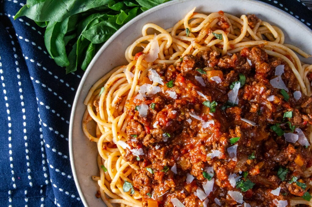 Overhead view of Slow Cooker Bolognese sauce with spaghetti, basil and parmesan cheese.