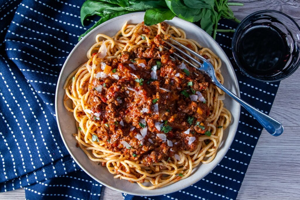 Overhead view of a plate of Slow Cooker Bolognese ragu with spaghetti, basil, parmesan and a glass of red wine.