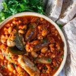 Overhead view of Slow Cooker Sausage Casserole in a bowl with fresh parsley and white crusty bread on the side.