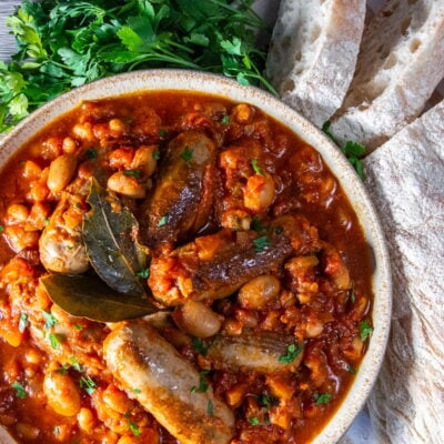 Overhead view of Slow Cooker Sausage Casserole in a bowl with fresh parsley and white crusty bread on the side.