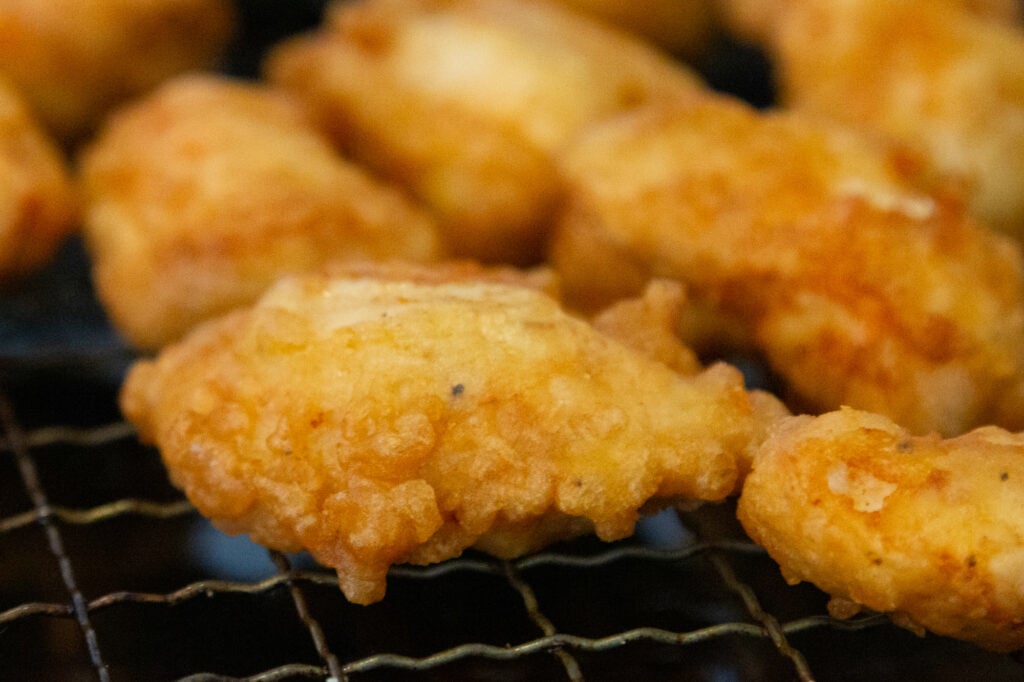 Close up view of a piece of battered chicken on a wire cooling rack.