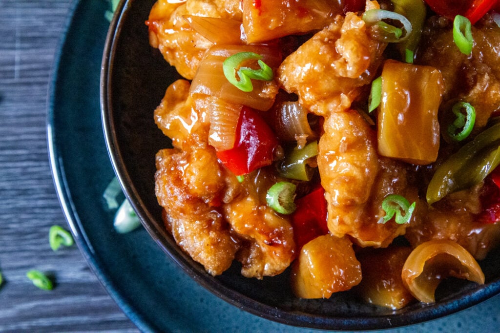 Closeup picture of Crockpot Sweet and Sour Chicken in a bowl with spring onion garnish.