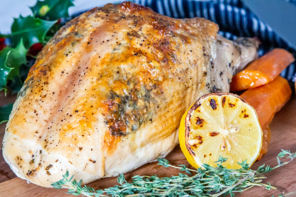 Crockpot Turkey Crown on a board with herbs and vegetables.