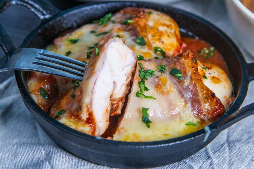 Hunter's Chicken cut open and held with a fork, over a skillet with melted cheese