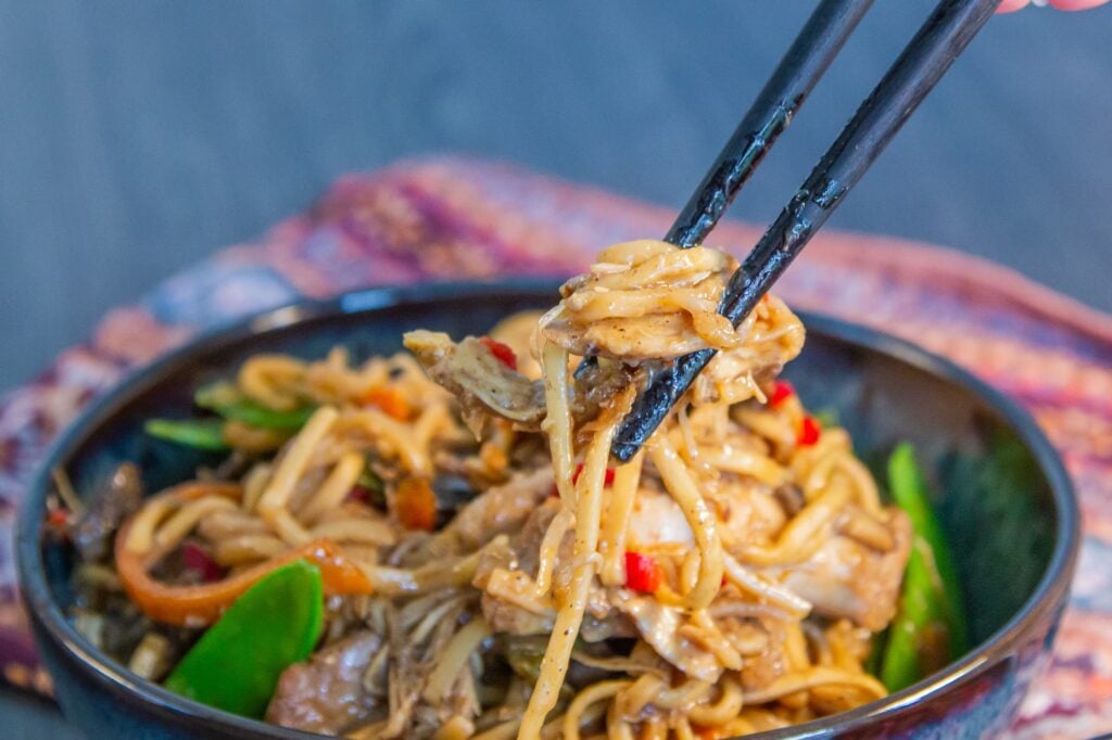 Slow Cooker Chicken Chow Mein in a bowl with chopsticks picking up some of the chicken noodles.