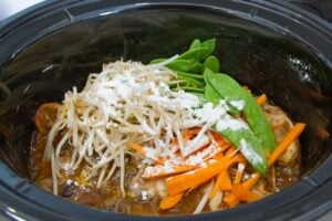 Process of adding vegetables to the slow cooker when making chow mein noodles.