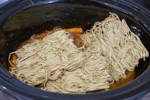 Process of adding noodles to the slow cooker with sauce and vegetables.