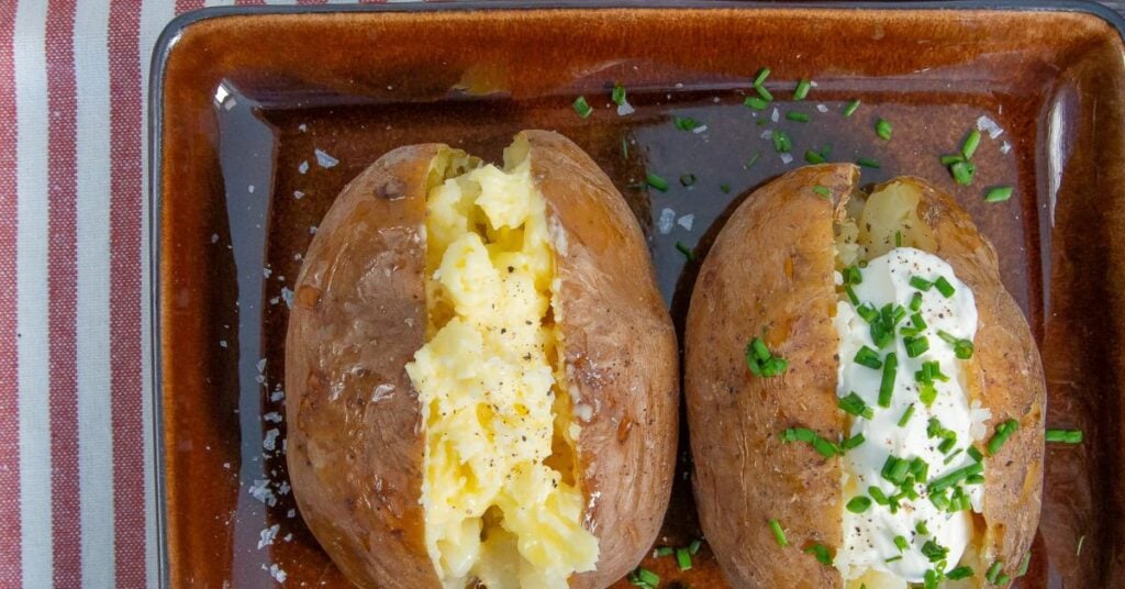Overhead view of Slow Cooker Jacket Potatoes with crispy skin. One has a sour cream and chive filling, the other butter.