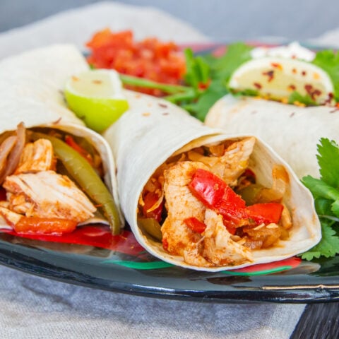 Slow Cooker Chicken Fajitas wrapped on a plate with lime and coriander.