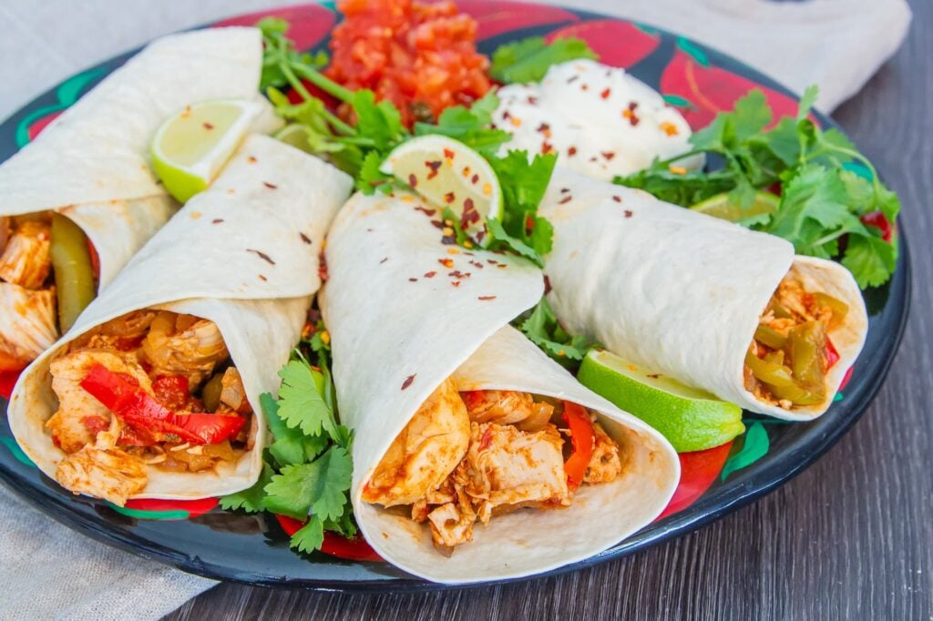 Plate of slow cooker chicken fajitas served with dips, coriander and lime.